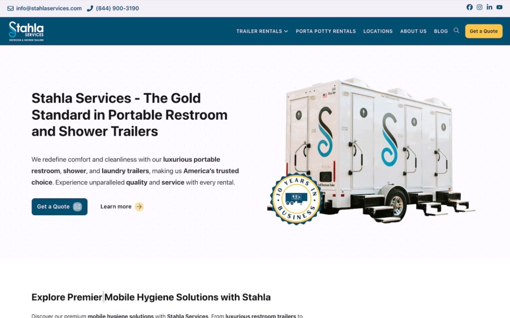 A parked trailer with several portable toilets labeled "Stahla Services" stands on a commercial site and advertises luxury portable toilet solutions.